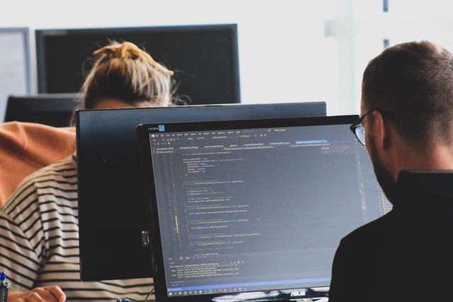 Two people sitting in front of their computers coding and provide customer support.