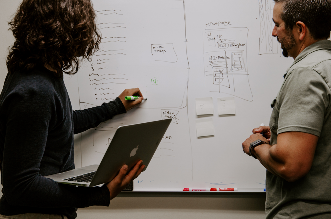 Two people in front of a whiteboard discussing a technology project.